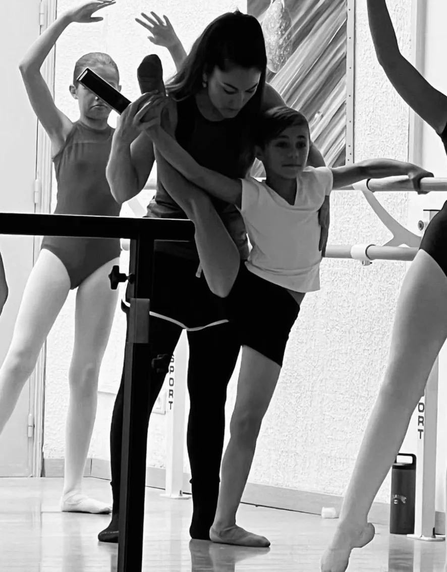 Professeure corrigeant un jeune danseur à la barre, photo en noir et blanc