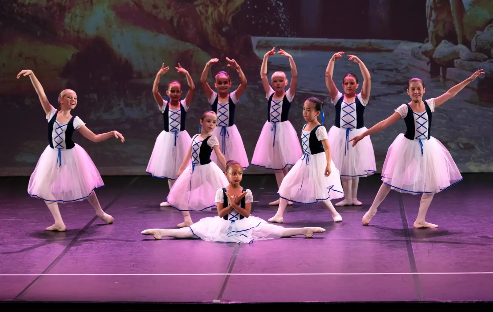 Groupe de jeunes danseuses classiques en tutus blancs et corsages bleu marine sur scène