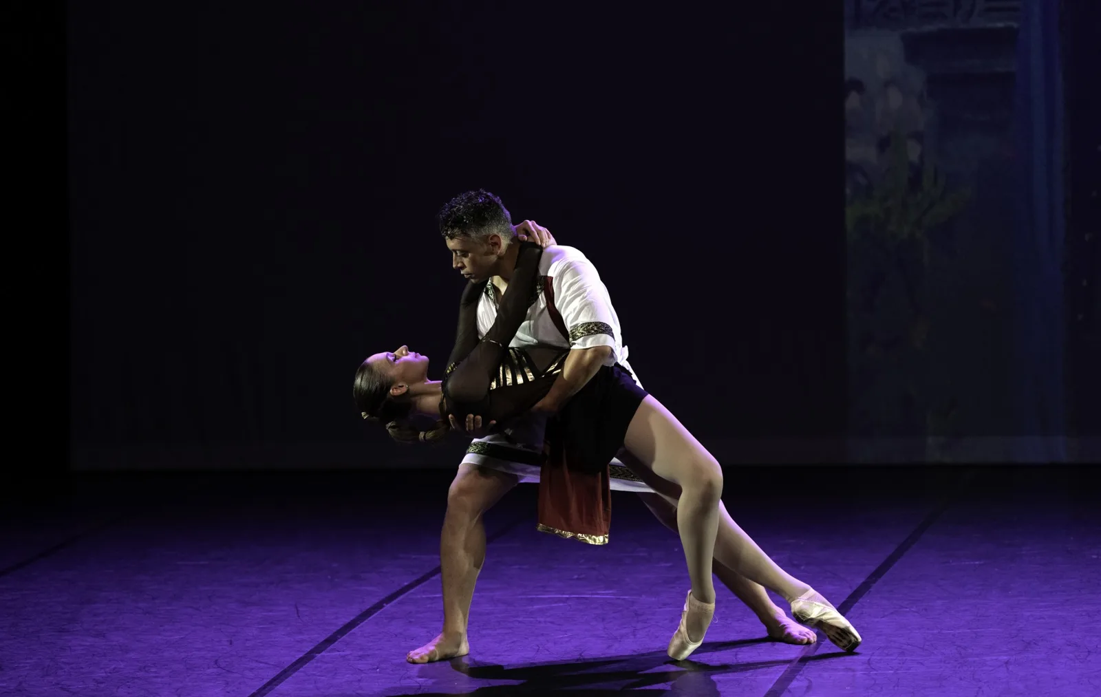 Pas de deux contemporain sur scène en lumière violette, costumes d'inspiration antique