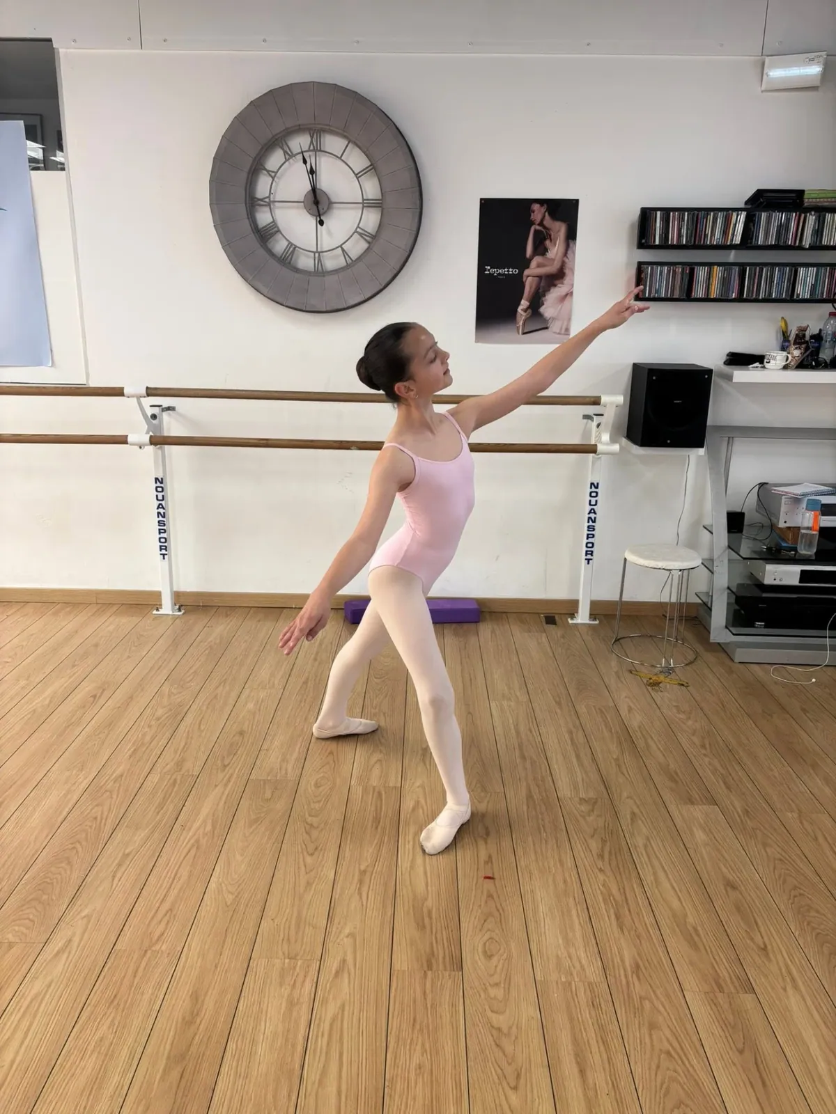 Jeune danseuse classique en tunique rose en pose devant la barre du studio