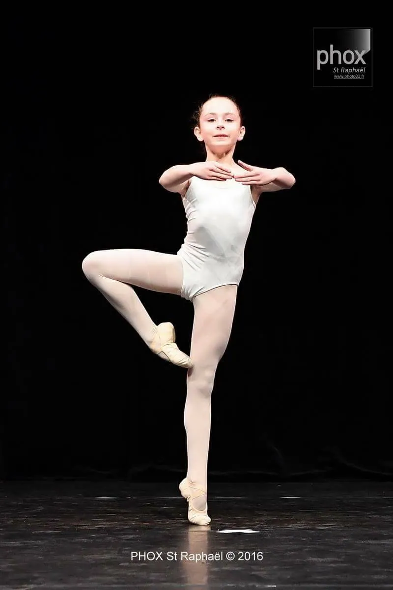 Jeune danseuse en justaucorps blanc en passé lors d'une variation classique