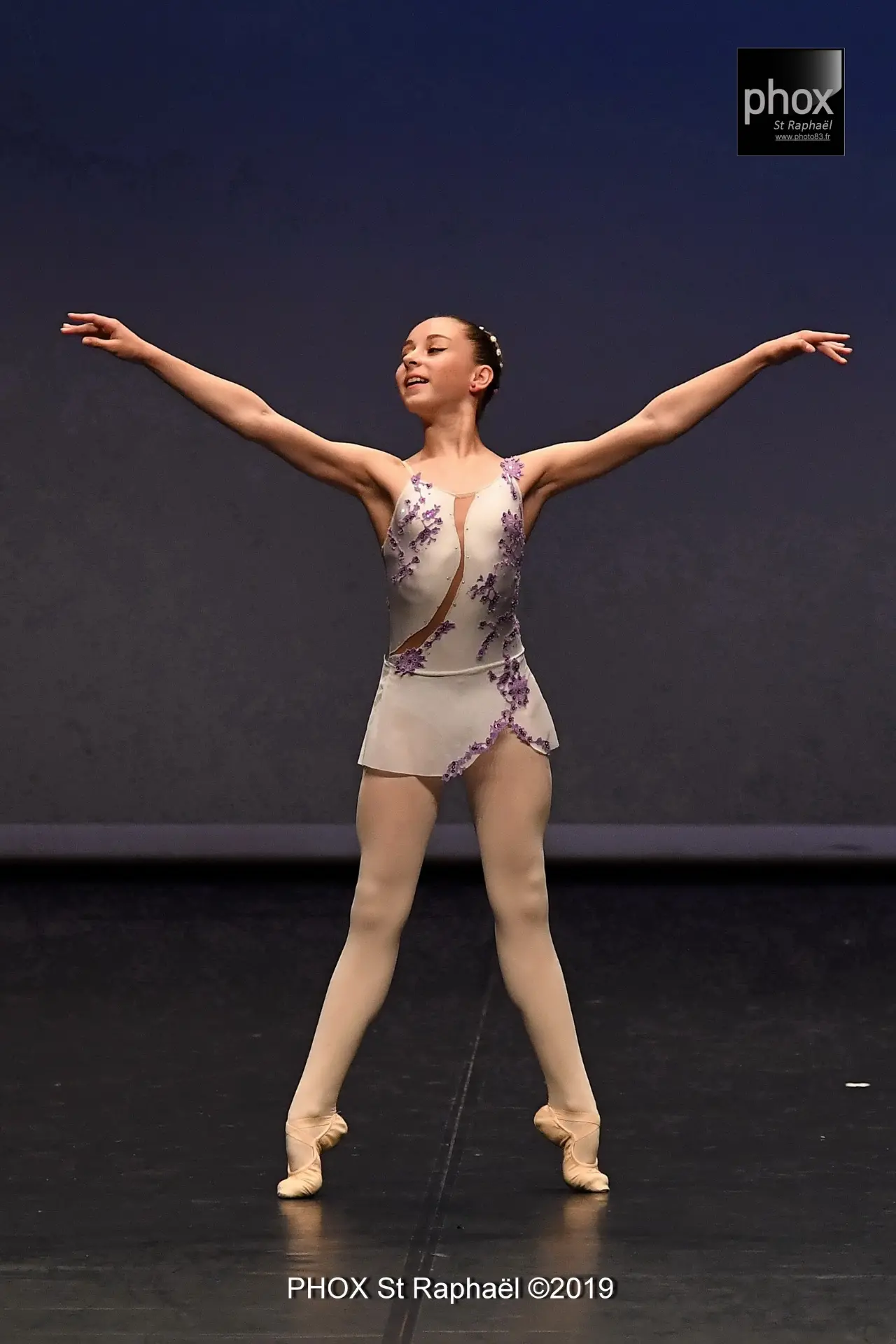 Jeune danseuse en variation classique sur scène, bras en seconde