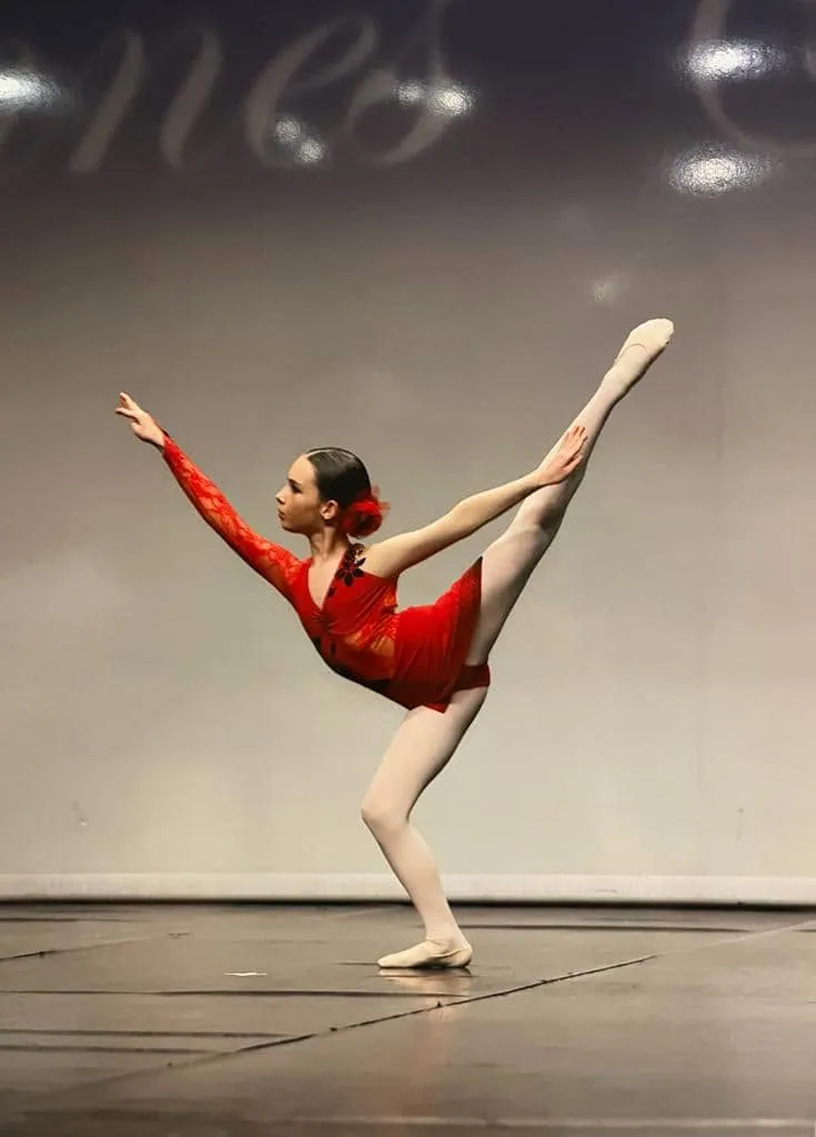 Élève en arabesque, variation en costume rouge sur scène de concours